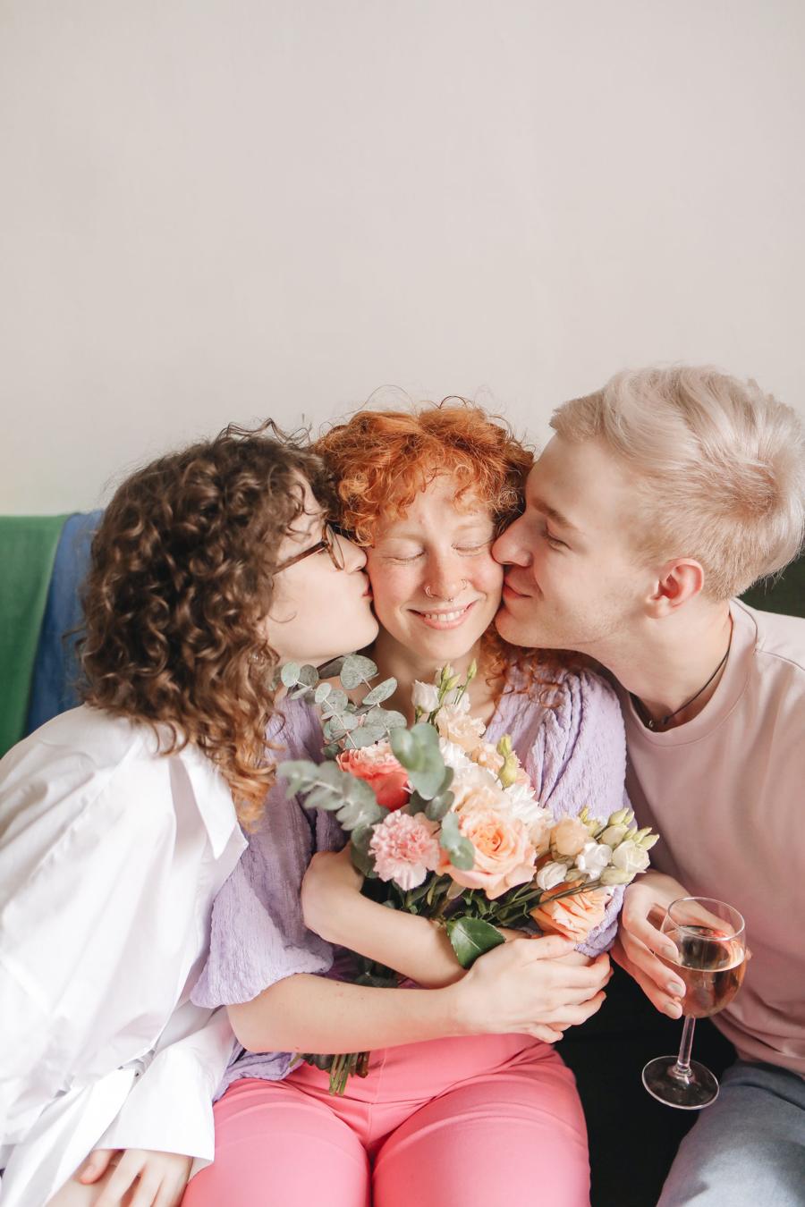 Three partners sharing an affectionate moment, one holding a bouquet